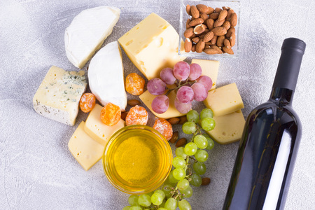 Snacks with wine - bottle, various types of cheeses, figs, nuts, honey, grapes on a white wooden backgroundの写真素材