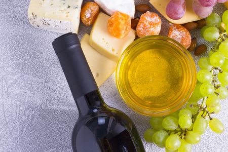 Snacks with wine - bottle, various types of cheeses, figs, nuts, honey, grapes on a white wooden backgroundの写真素材