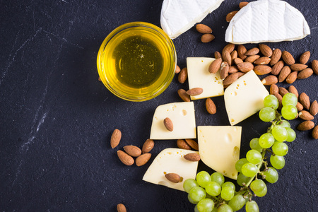 Snacks with wine - various types of cheeses, figs, nuts, honey, grapes on a black stone backgroundの写真素材