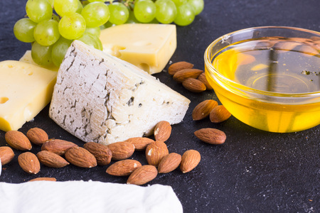 Snacks with wine - various types of cheeses, figs, nuts, honey, grapes on a black stone backgroundの写真素材