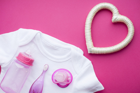 Newborn baby story. T-shirt and children's toys, scissors, baby bottle, nipple, hairbrush on red background. Top viewの写真素材