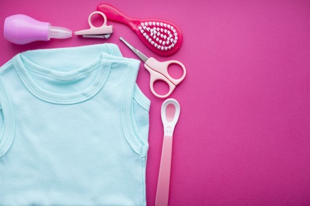 Newborn baby story. T-shirt and children's toys, scissors, baby bottle, nipple, hairbrush on red background. Top viewの写真素材