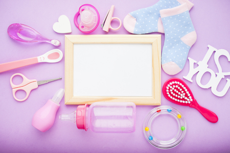 Newborn baby story. Frame with copyspace and children's toys, scissors, baby bottle, nipple, hairbrush on violet background. Top viewの写真素材