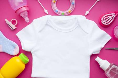 Newborn baby story. T-shirt and children's toys, scissors, baby bottle, nipple, hairbrush on red...