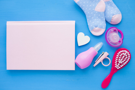 Newborn baby story. Notepad with copyspace and children's toys, scissors, baby bottle, nipple, hairbrush on blue background. Top viewの写真素材