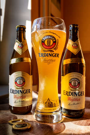 Erdinger beer is poured in a branded beer glass and two bottles