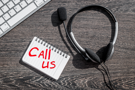 operator headset, notebook and keyboard for contact us feed back call center workdesk wooden background top viewの写真素材