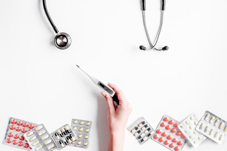 Medical equipment with stethoscope and pills in doctors office on white desk background top view