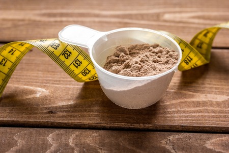 protein powder for fitness nutrition to start training and measure tape wooden backgroundの写真素材