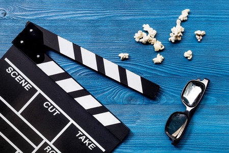 Watching the film. Movie clapperboard, sunglasses and popcorn on blue wooden table background top viewの写真素材