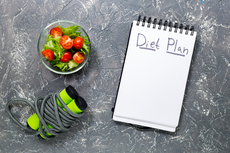 Notebook for diet plan, salad with fresh products and jump rope on stone table top view mock upの写真素材
