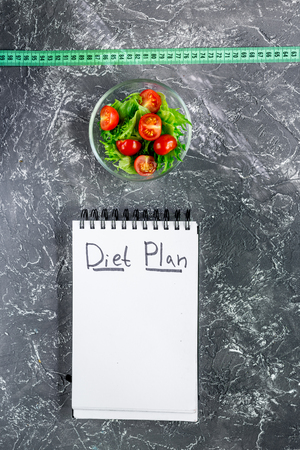 Notebook for diet plan, salad and measuring tape on grey stone table top view mock up.の写真素材