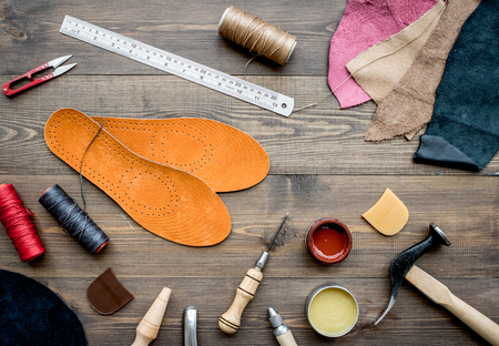 Set of cobbler tools on brown wooden desk background top view.