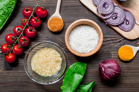 rice, spices and vegetables for paella on wooden kitchen desk background top viewの写真素材