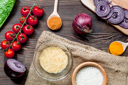 rice, spices and vegetables for paella on wooden kitchen desk background top viewの写真素材