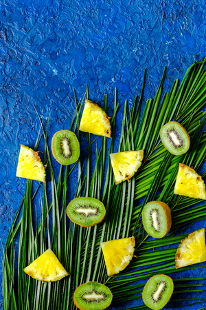 Concept of summer tropical fruits. Pineapple, cocount and palm branch on blue table background top view.の写真素材