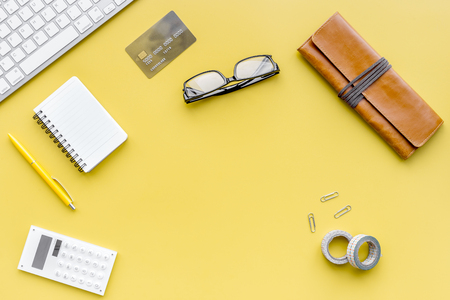 Modern office worker workplace with keyboard, notebook, glasses and pencil case on yellow table background top view.の写真素材