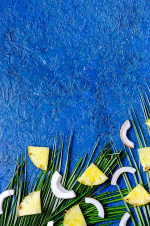 Concept of summer tropical fruits. Pineapple, cocount and palm branch on blue table background top viewの写真素材