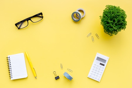 Manager workplace in office with calc, glasses and notebook on yellow table background top view.の写真素材