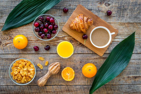 Light tasty breakfast. Muesli, oranges, cherry, french croissant and milky coffee on wooden table background top viewの写真素材