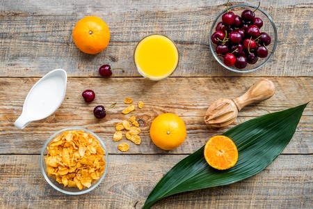 Preparing healthy summer breakfast. Muesli, milk, oranges, cherry, on wooden table background top viewの写真素材