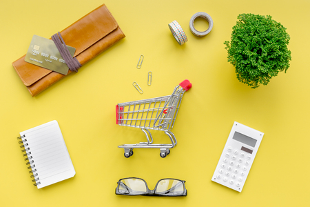 Shopping in online store. Bank card nearby purse, calculator and shopping cart on yellow background top viewの写真素材