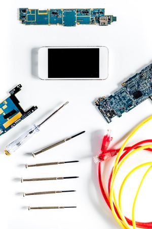 Parts of disassembled cell phone and screwdrivers on white background top view