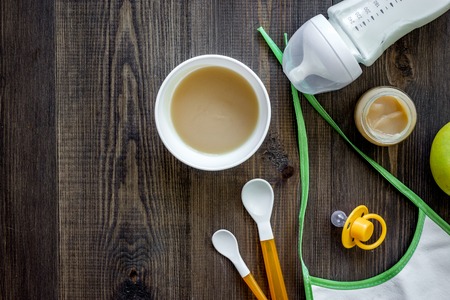 Preparing to feed baby. Puree, spoon, nipple, bottle and bib on dark wooden table background top view copyspaceの写真素材