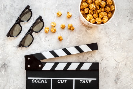 Watching film. Clapperboard, glasses and popcorn on grey stone background top view.の写真素材