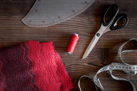 Clothing designer workplace. Fabric. measuring tape, thread and sciccors on dark wooden table...