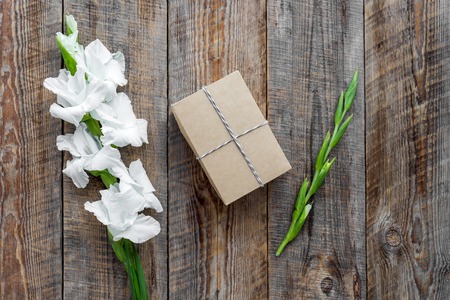 Gift box wrapped in craft paper near flower gladiolus on wooden tableの写真素材