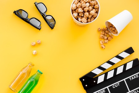 Snacks for film watching. Popcorn and soda near clapperboard, glasses on yellow background top view.の写真素材