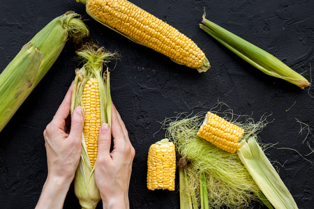 Woman's hands clean corn cob. Black stone background top view.