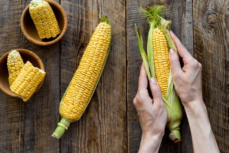 Woman's hands clean corn cob. Black stone background top view.