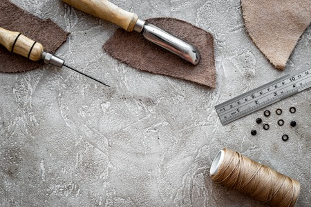 Leather craft. Tanner's tools on grey stone background top view.