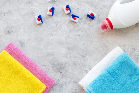 Laundry. Dry and liquid detergents near clean towel on grey stone background top view.