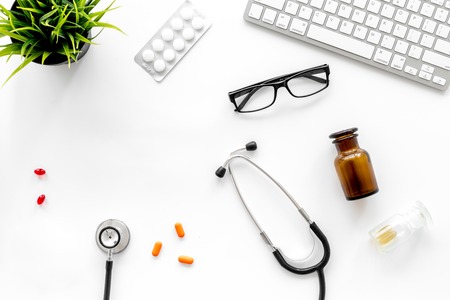 An appointment. Doctors workplace in clinic. Stethoscope and pills near keyboard on white background top view copyspaceの写真素材
