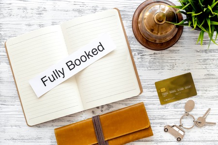 Book hotel. Service bell and notebook with word fully booked at the reception on light wooden table top viewの写真素材