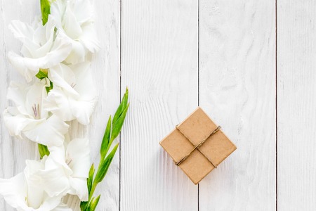 Celebration accessories. Box in kraft paper near flower gladiolus on white wooden table top view copyspaceの写真素材