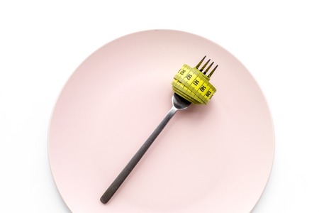 Losing weight. Strict diet. Empty plate and measuring tape on fork instead food on white background top view mockupの写真素材