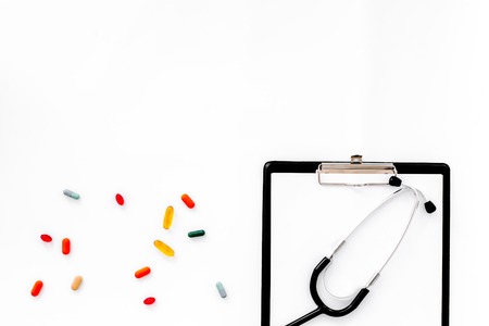 Doctors workplace in clinic. Accessories. Clip pad, stethoscope, colored pills on white background top view copyspaceの写真素材
