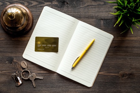 Book hotel. Service bell and notebook at the reception on dark wooden table top viewの写真素材