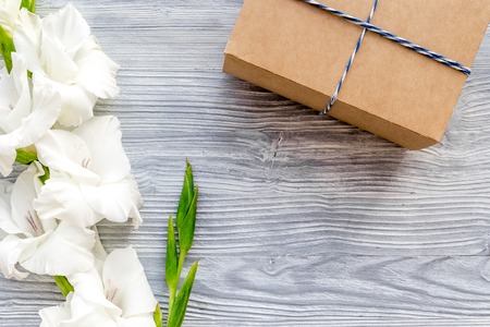 Celebration accessories. Box in kraft paper near flower gladiolus on light wooden table top view.の写真素材