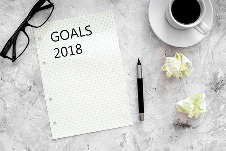 Goals list for 2018. Sheet of paper near pen, glasses and cup of coffee on grey stone background top view mockupの写真素材