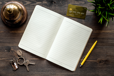 Book hotel. Service bell and notebook at the reception on dark wooden table top view mockupの写真素材