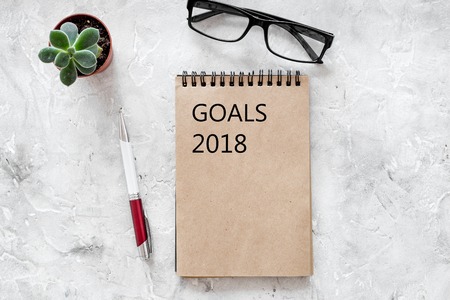 Words Goals for 2018 writting in notebook near glasses on grey stone background top view mockup.