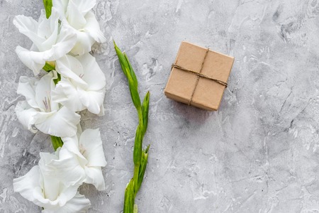 Gift box wrapped in craft paper near flower gladiolus on grey stone background top view.の写真素材