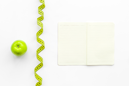 Slimming diet dairy. Notebook, apple and measuring tape on white background top view.の写真素材
