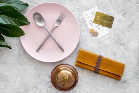 Meal is over. Bill, wallet and bank card near plate with crossed spoon and fork on grey stone table top view.の写真素材