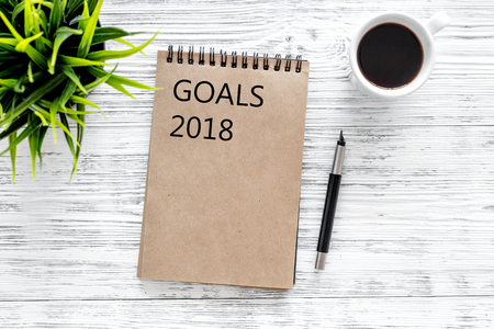 Words Goals for 2018 writting in notebook near glasses and cup of coffee on grey wooden background...